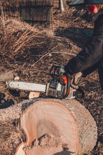 A young woman launches a chainsaw for cutting wood in the countryside