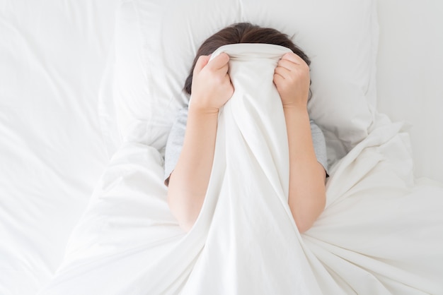 Young woman laying in bed hiding her face