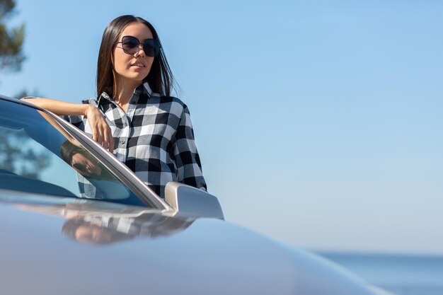 Young woman leaning convertible on the road at daytime