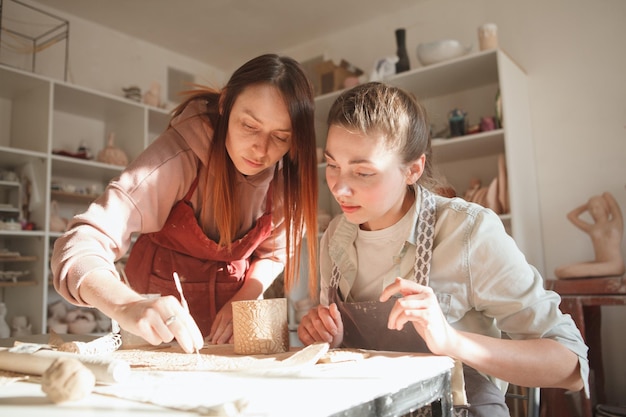 Young woman learning pottery from female ceramist