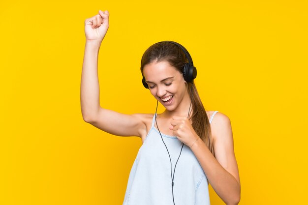 Photo young woman listening music isolated on yellow wall celebrating a victory