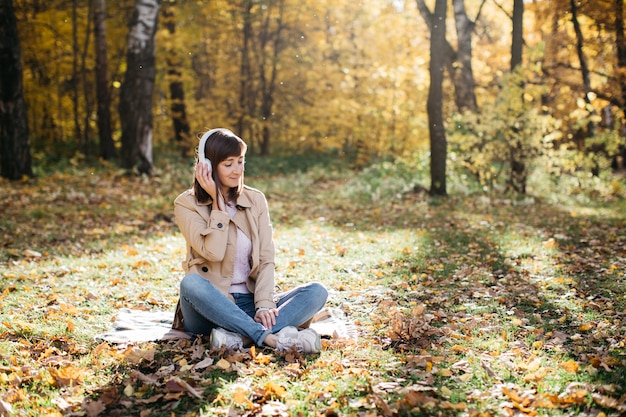 Young woman listening to music with headphones in the autumn forest