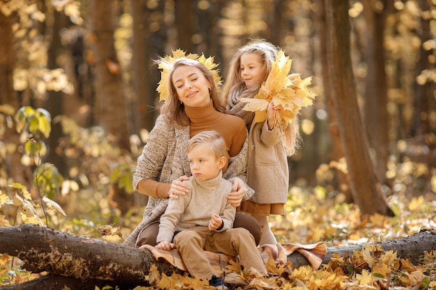 Young woman and little girl and boy walking in autumn forest. Woman, her daughter and son playing and having fun. Girl wearing brown dress.