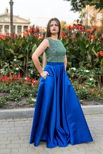 Young woman in long dress posing near flowerbed