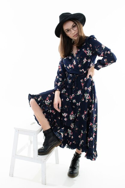 Young woman in a long floral dress with a hat poses for the camera