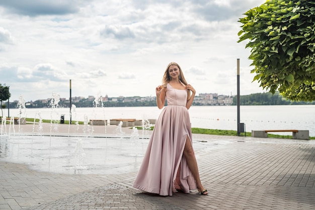 Young woman in long pink evening dress standing alone near lake at city park Lifestyle concept outdoor