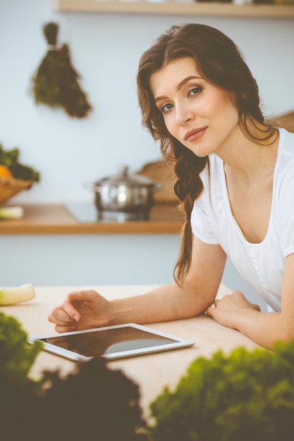 Young woman looking for a new recipe for cooking in a kitchen. Housewife is making online shopping by tablet computer and credit card.