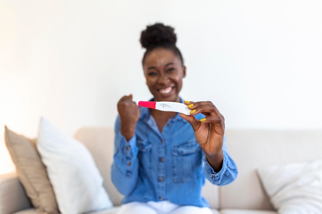 Young woman looking at pregnance test in happiness Finally pregnant Attractive black women looking at pregnancy test and smiling while sitting on the sofa at home