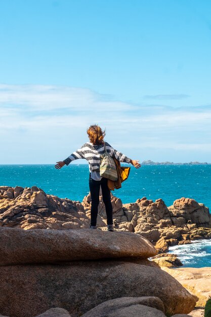 A young woman looking at the sea along Lighthouse Mean Ruz, port of Ploumanach, in the town of Perros-Guirec, Cotes-d'Armor, in French Brittany, France.