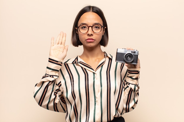 Young woman looking serious, stern, displeased and angry showing open palm making stop gesture