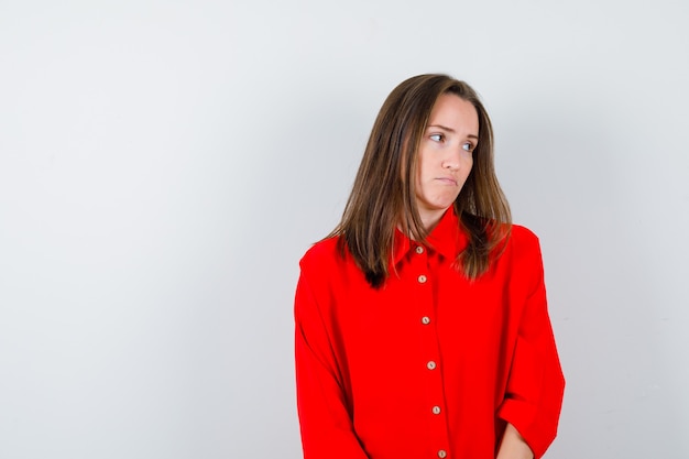 Young woman looking to the side in red blouse and looking aggrieved , front view.