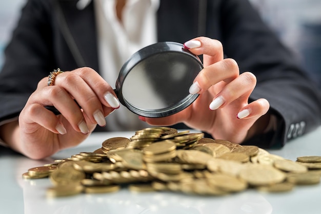 Young woman looking through magnifying glass at rising coin graph