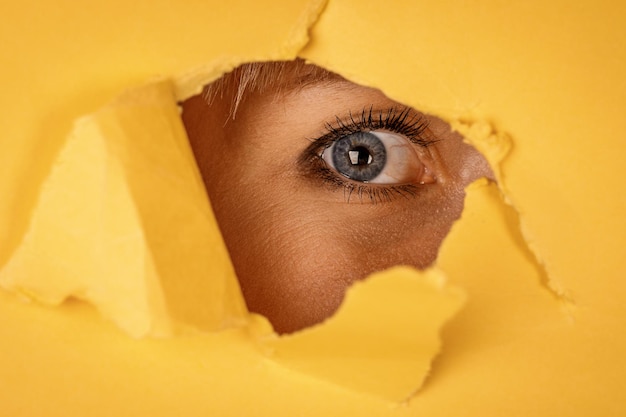 Young woman looking through torn yellow paper