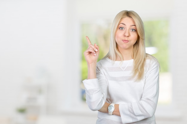 Young woman looking up and pointing at blank wall