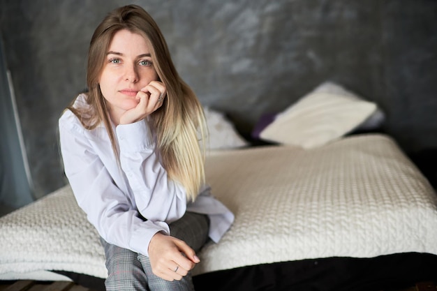 A young woman looks thoughtfully into the camera on the background of the bed Domestic violence concept