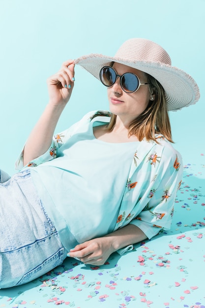 Young woman lying down in summer clothes with pink straw hat and big round glasses