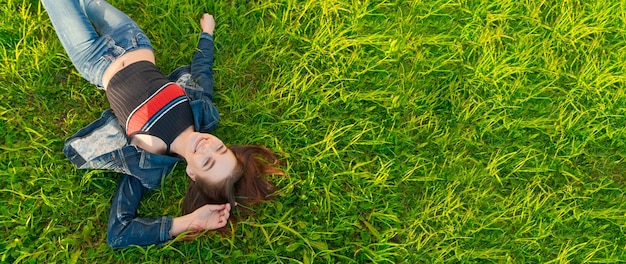 Young Woman lying in nature on green grass in park relaxing smiling her red