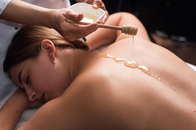 Young woman lying on the table and getting spa procedure massage with honeyed in dark room