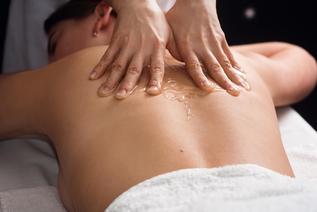 Young woman lying on the table and getting spa procedure massage with honeyed in dark room