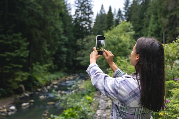 A young woman makes a photo in the mountains in the forest on a smartphone