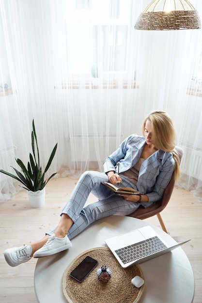 Young woman making notes in notebook sitting at workplace at home remote work