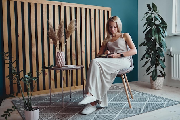 Young woman making notes in notebook sitting at workplace at home remote work