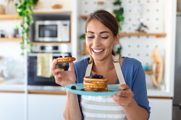 Young woman making pancakes at kitchen Young housewife enjoying blueberry pancakes for breakfast