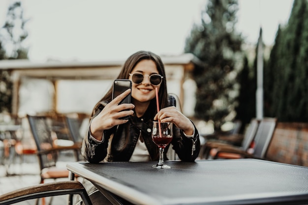 Young woman making self portrait using smartphone. Girl making selfie. Woman in cafe. Woman alone. Self portrait in cafe outdoors. smile. smilimg. gadget. self portrait. coffe break. coffee time