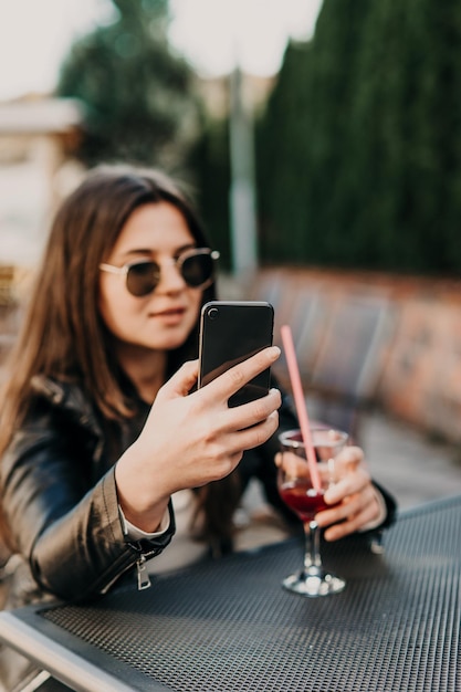 Young woman making self portrait using smartphone. Girl making selfie. Woman in cafe. Woman alone. Self portrait in cafe outdoors. smile. smilimg. gadget. self portrait. coffe break. coffee time