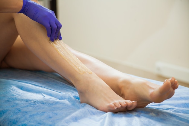 Young woman making sugaring hair removal procedure at beauty salon