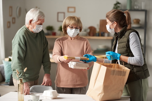 Photo young woman in mask as a volunteer delivering food to senior couple to home during pandemic