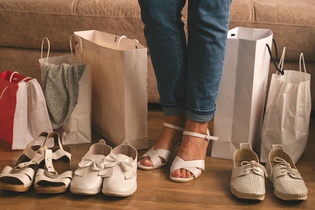 Young woman measure new shoes  and standing between shopping bags at home, delivery and shopping concept