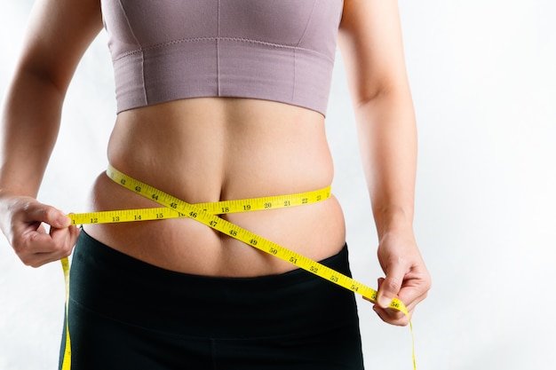 Young woman measuring her excessive belly fat waist with measure tape, woman diet lifestyle concept