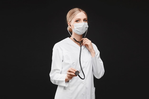 Young woman in medical uniform and protective mask using a stethoscope