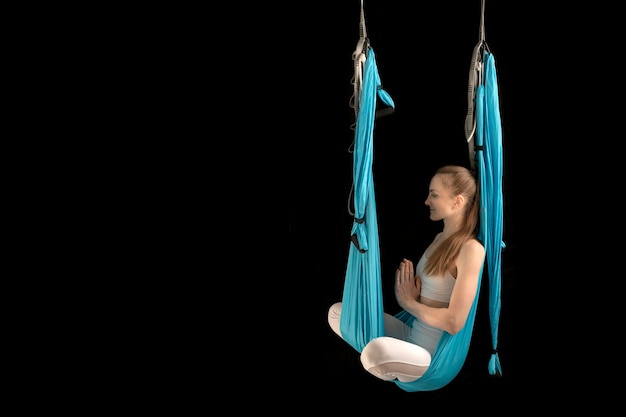 Young woman meditates sitting in the lotus position in sports hammock Antigravity yoga Fly Yoga Copy space