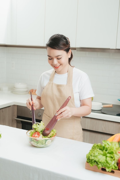 Young woman mixing fresh salad standing near desk