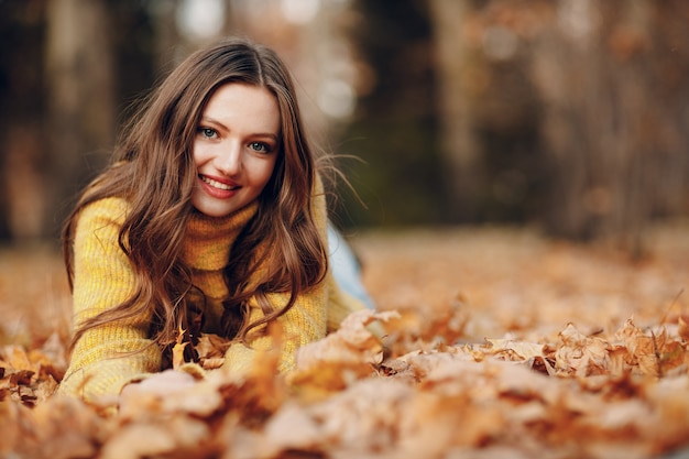 Young woman model in autumn park with yellow foliage maple leaves. Fall season fashion.