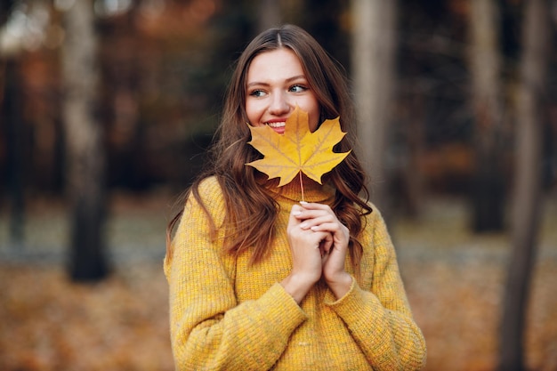 Young woman model in autumn park with yellow foliage maple leaves Fall season fashion