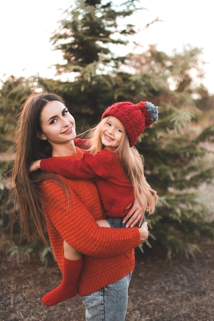 Young woman mom spend time with daughter kid girl wear red knit sweater and hat over tree outdoor Motherhood Autumn season Happiness