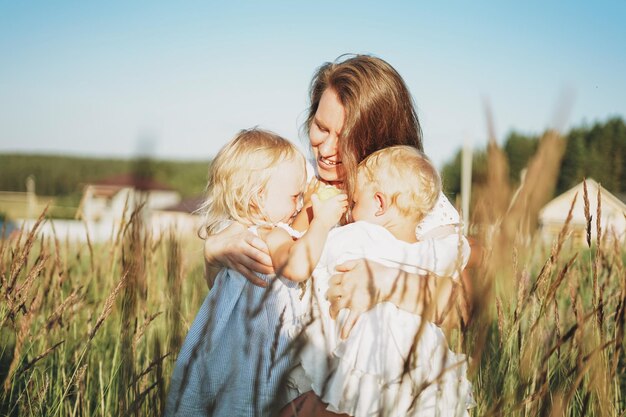 Young woman mom with baby girls twins on hands hug in backyard of the cottage in sunset light