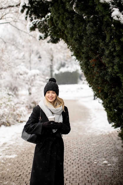 Young woman n warm clothes enjoying in snow with takeaway coffee cup