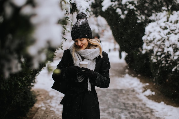 Young woman n warm clothes enjoying in snow with takeaway coffee cup