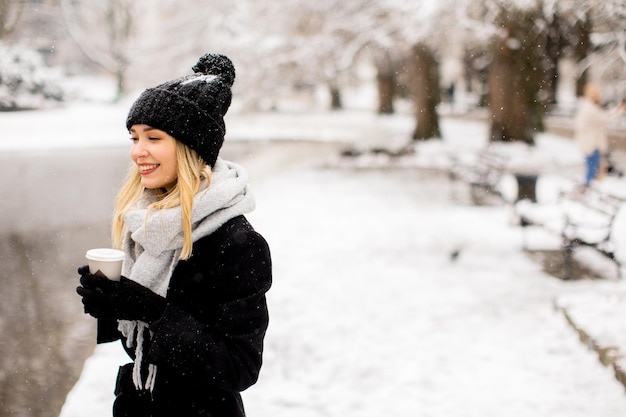 Young woman n warm clothes enjoying in snow with takeaway coffee cup