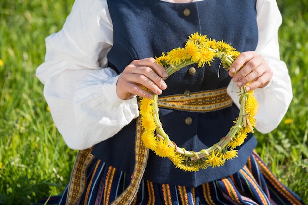 Young woman in national clothes wearing yellow dandelion wreath in spring field springtime