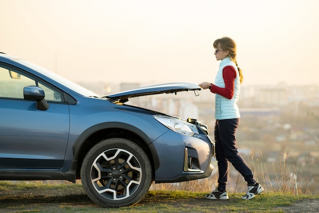 Young woman opening bonnet of broken car