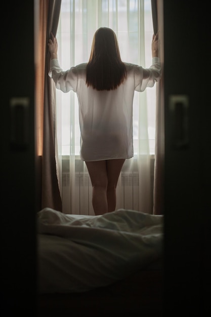 Young woman opening curtains in a bedroom