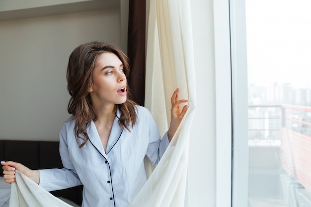 Young woman opens curtains to look at the view