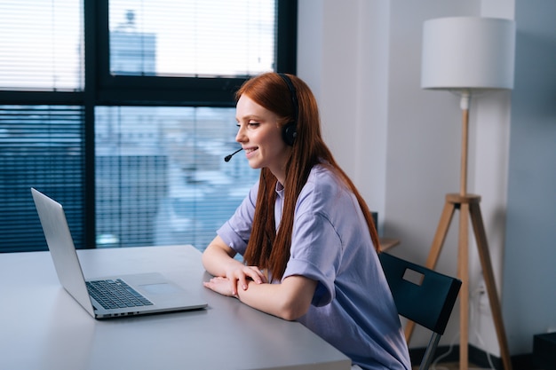 young woman operator using headset and laptop during customer support at home office