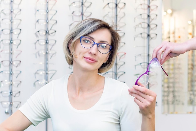 Young woman in optic store choosing new glasses with optician glasses in the store of optics A woman chooses glasses Emotions Ophthalmology