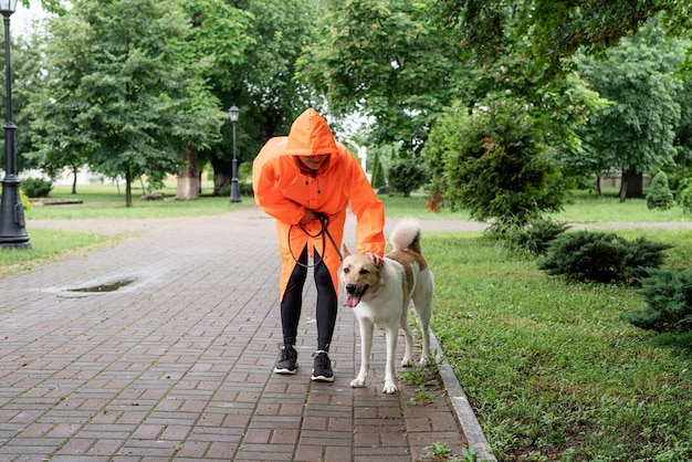 Young woman in orange raincoat walking with her dog in a park